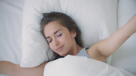 Young-woman-wakes-up-in-bed-in-the-morning-smiling-raises-her-hands